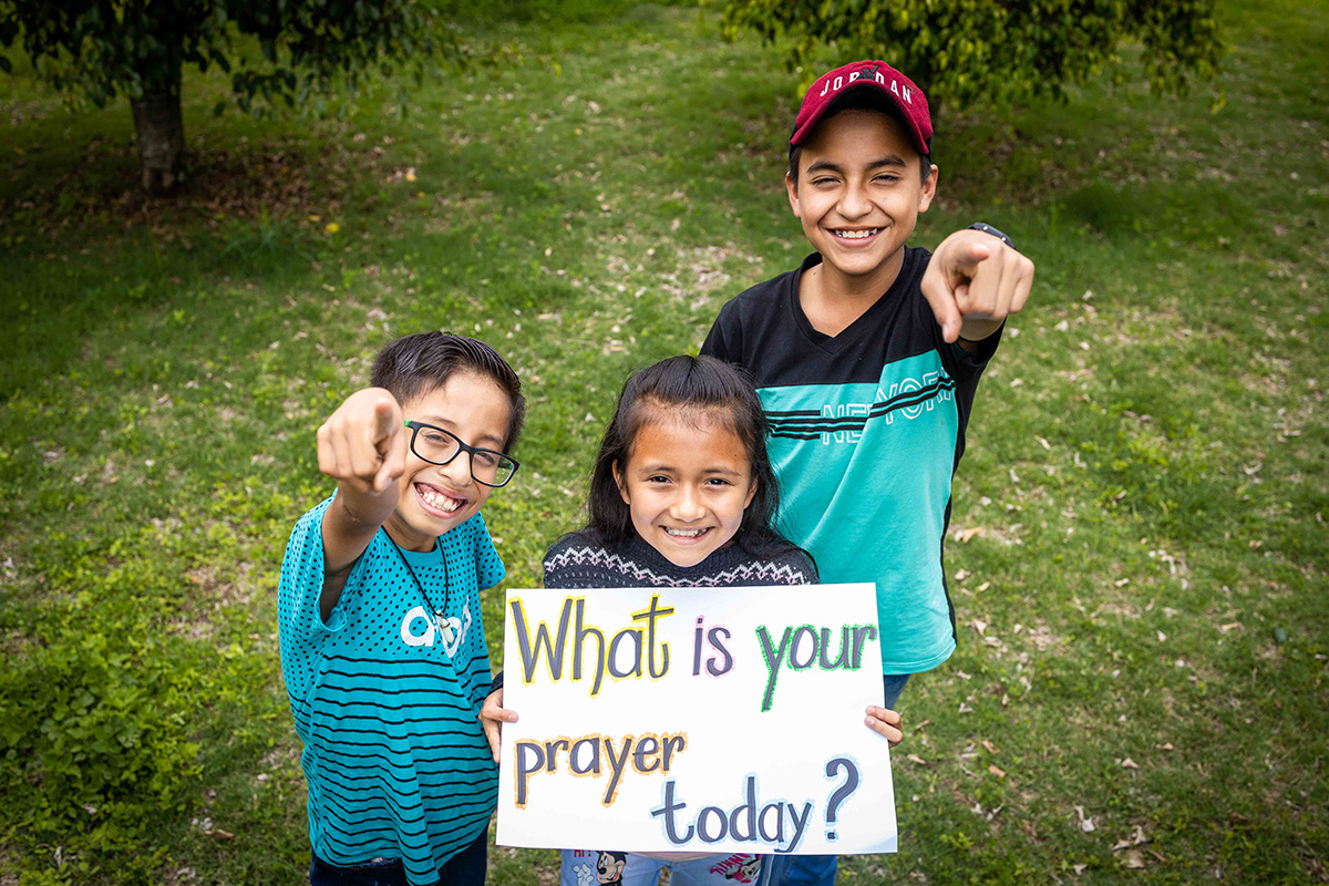 3 children hold a sign that says "What is your prayer today?"