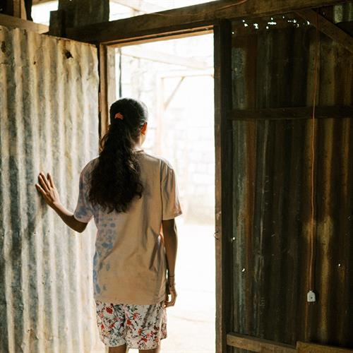 a teen girl stands in the doorway of her home