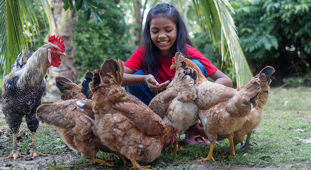 Girl crouching with group of chickens