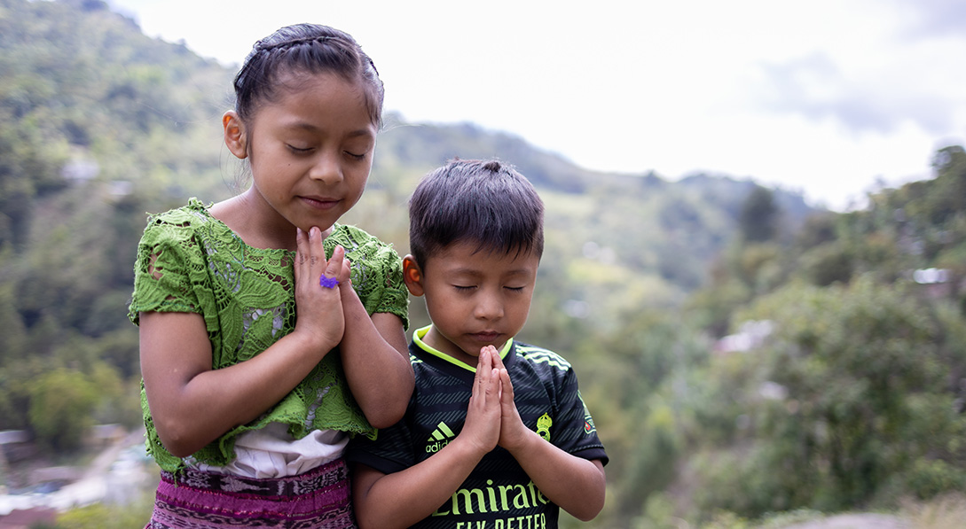 Two children praying in front of mountains
