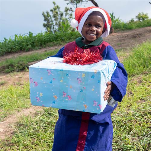 Child delivering present that is blue with a santa hat on