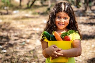 a girl holds a bucket of fresh vegetables