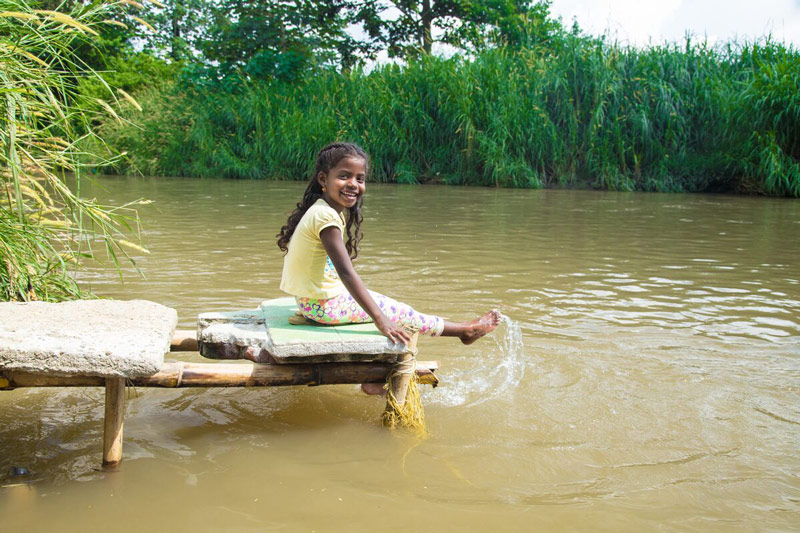 A girl hangs her feet in water off of a dock