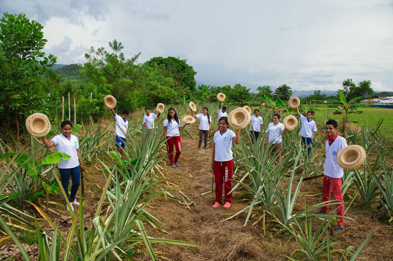 Girls and boys who are learning to farm wave their straw hats to welcome visitors