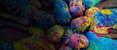 Children covered in colorful powder lie on their backs in a circle with their heads touching