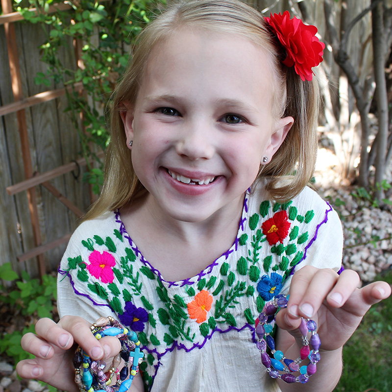 A young girl holds bracelets that she sells to help fundraise.