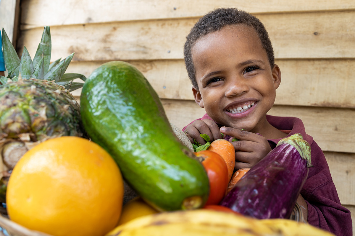 a boy smiles with a table full of fresh fruits and vegetables