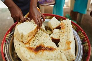 An Ethiopian woman uses a knife to cut into a large loaf of dabo.