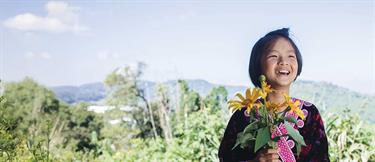 Smiling girl holding bouquet of flowers in field with mountains behind her