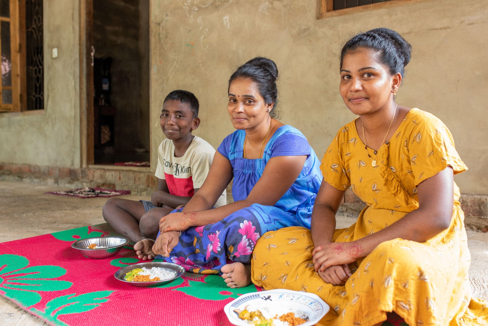 Dushiyandini is at home sitting on the ground on a mat with her daughter, Yadusha, and her son, Arikaran. They are about to eat the meal that Dushiyandini prepared for them.