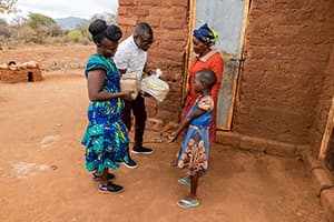Catherine and her daughter, Stella, receive food supplies from local church staff outside their home in Kenya.