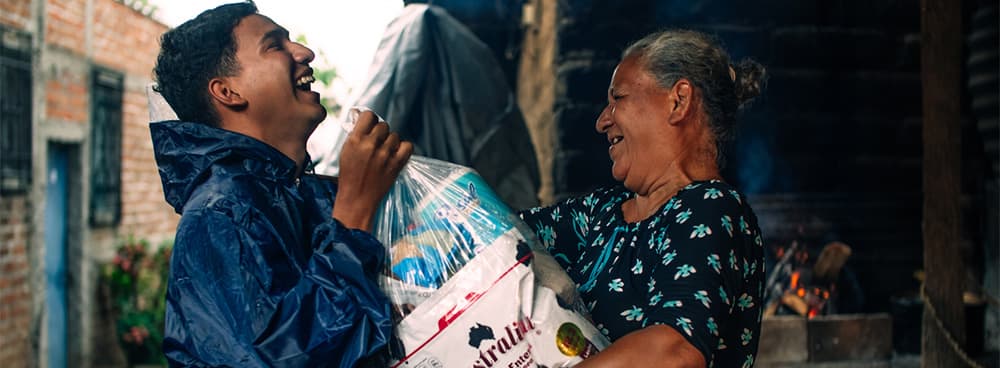 Young man giving an armload of food to an elderly woman. Both are laughing with joy