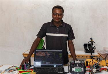 a teenage boy stands behind a sewing machine