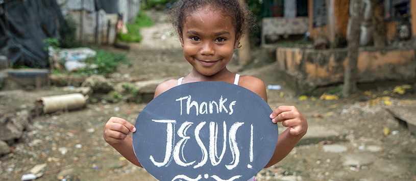 a young girl holds a sign that says Thanks Jesus