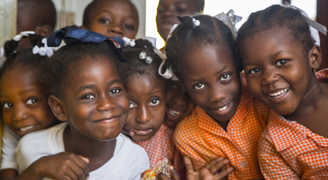Young girls at a school in Haiti gather together and smile for the camera.