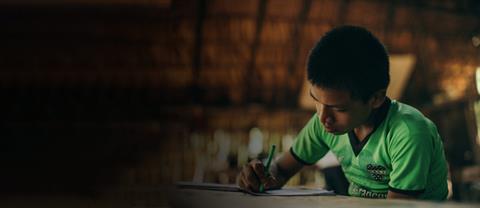 A boy living in Peru sits at a desk writing a letter