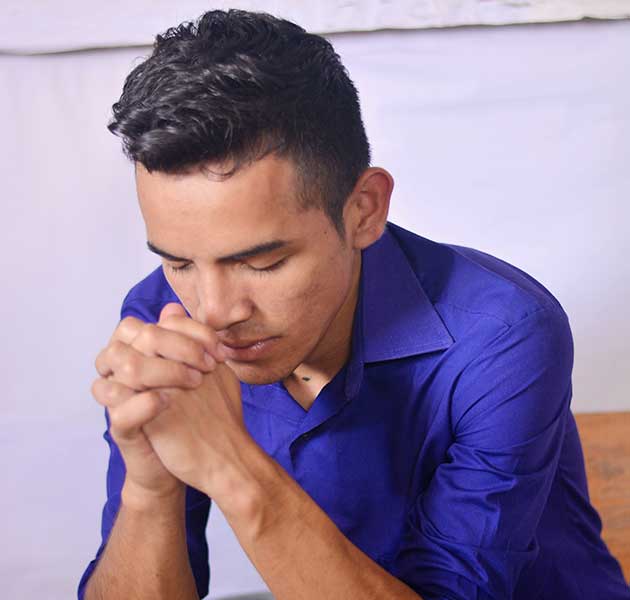 A teen boy prays with his hands folded