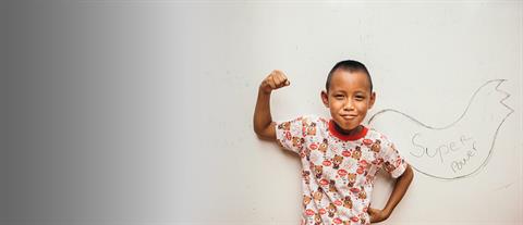 A young boy flexing his bicep with the words super power written out on a board behind him