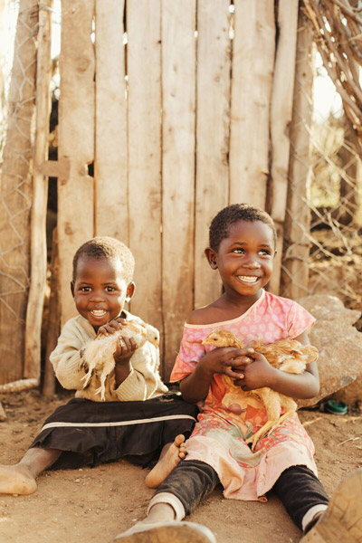 Two children smiling and sitting on ground