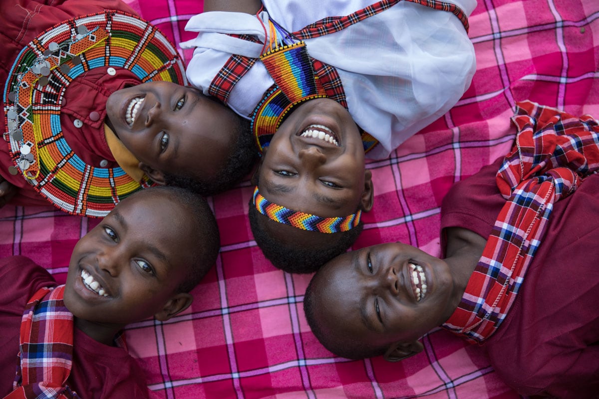 Kids laying on a red plaid blanket with their heads together smiling at the camera