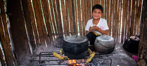 A boy peels a plantain over a two pots on a firepit