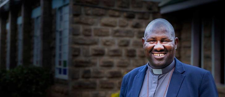 Pastor standing in front of brick wall smiling at camera