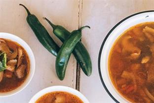 Three bowls of wild mushroom soup sit on a table next to three hot peppers