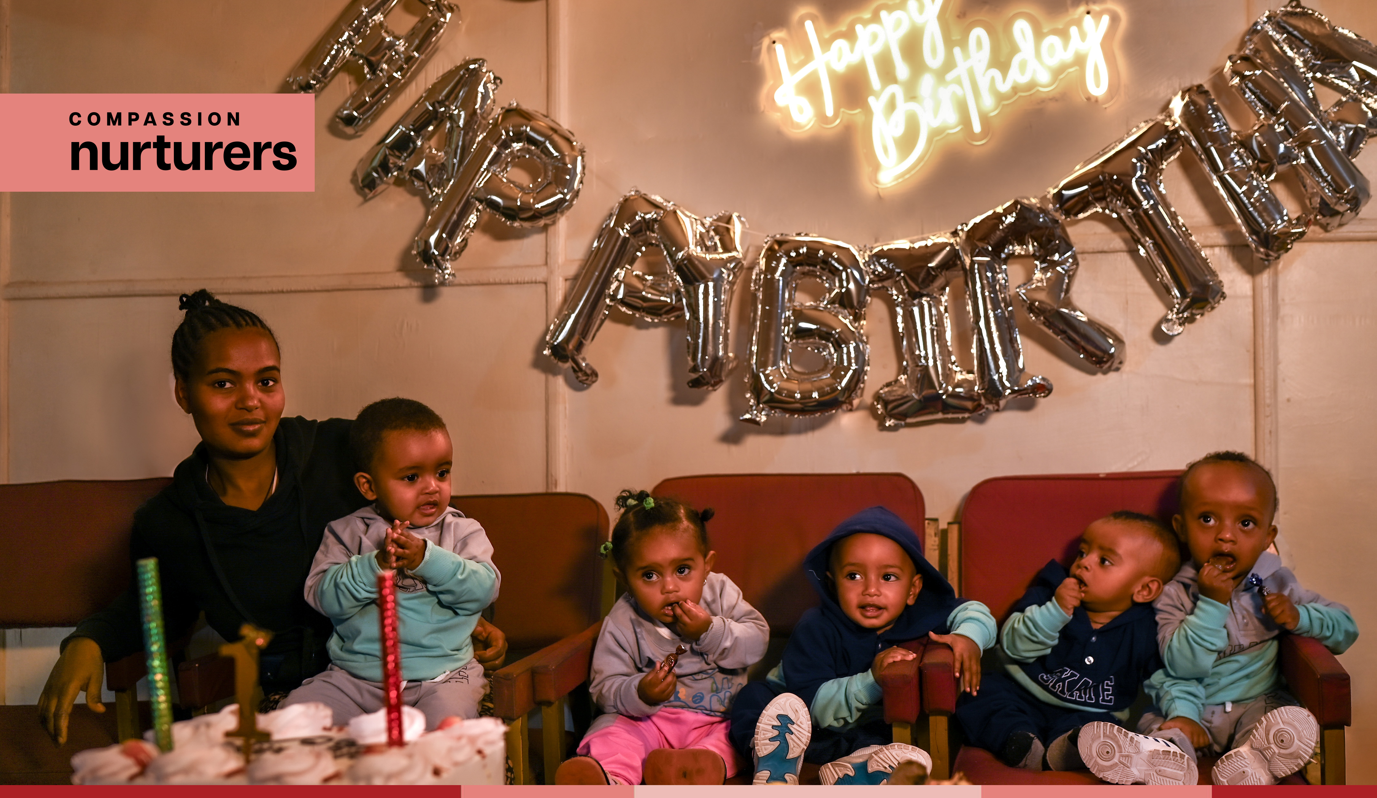 A mother sits on a chair beside five young children at a birthday party