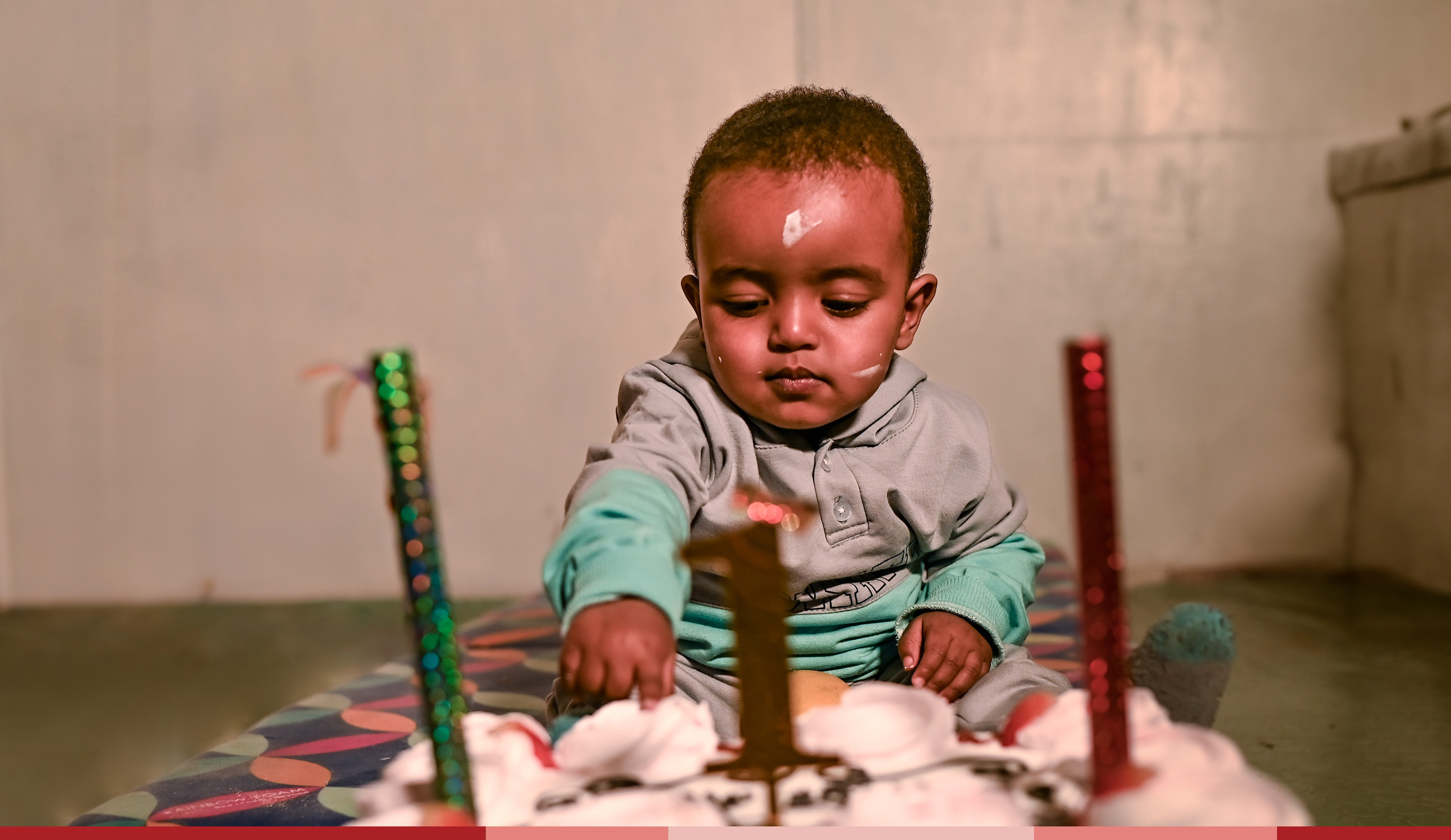 A one year old sits in front of a cake and candles at a birthday party