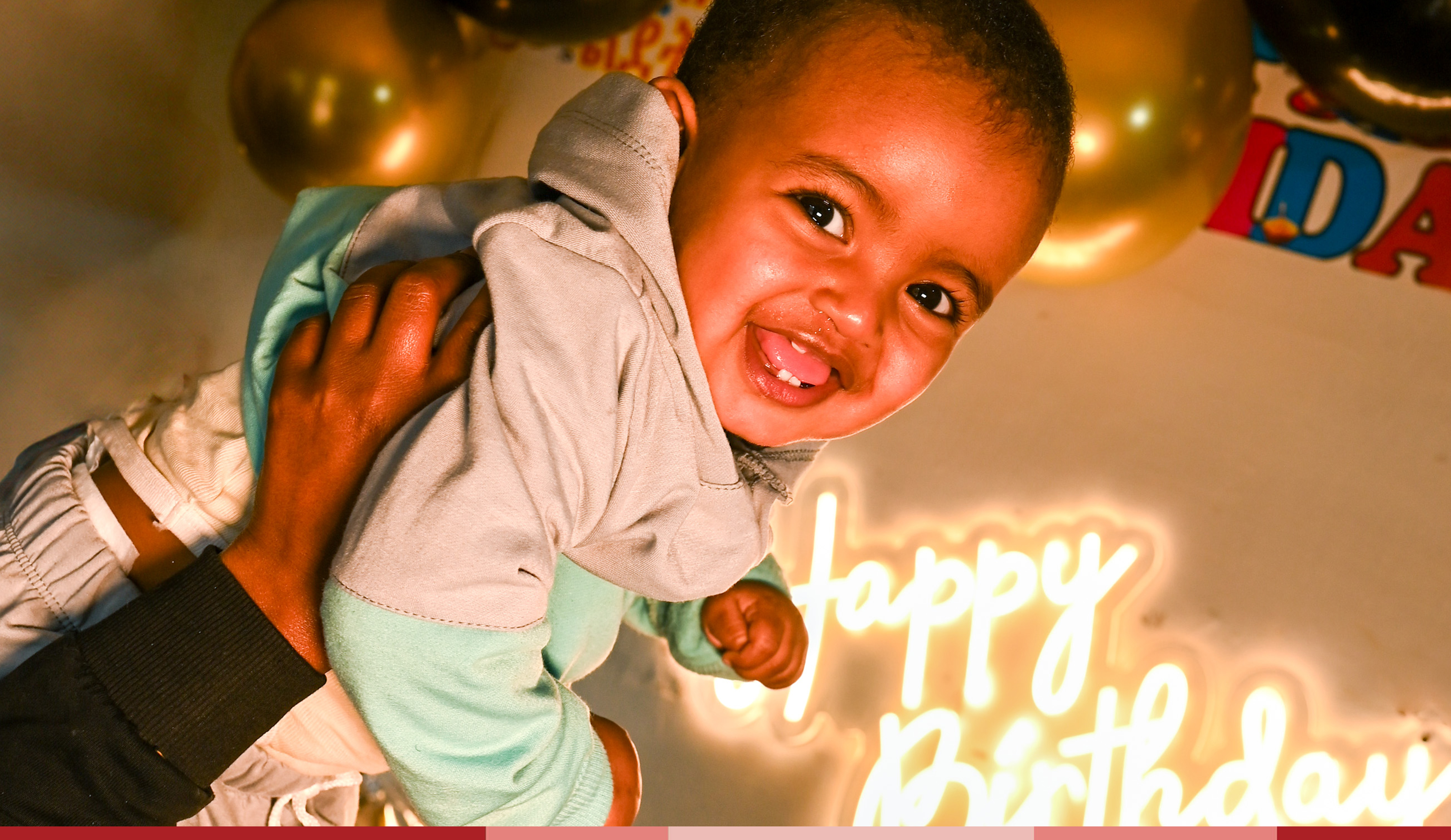 A smiling one year old is being held up in front of a sign that says happy birthday