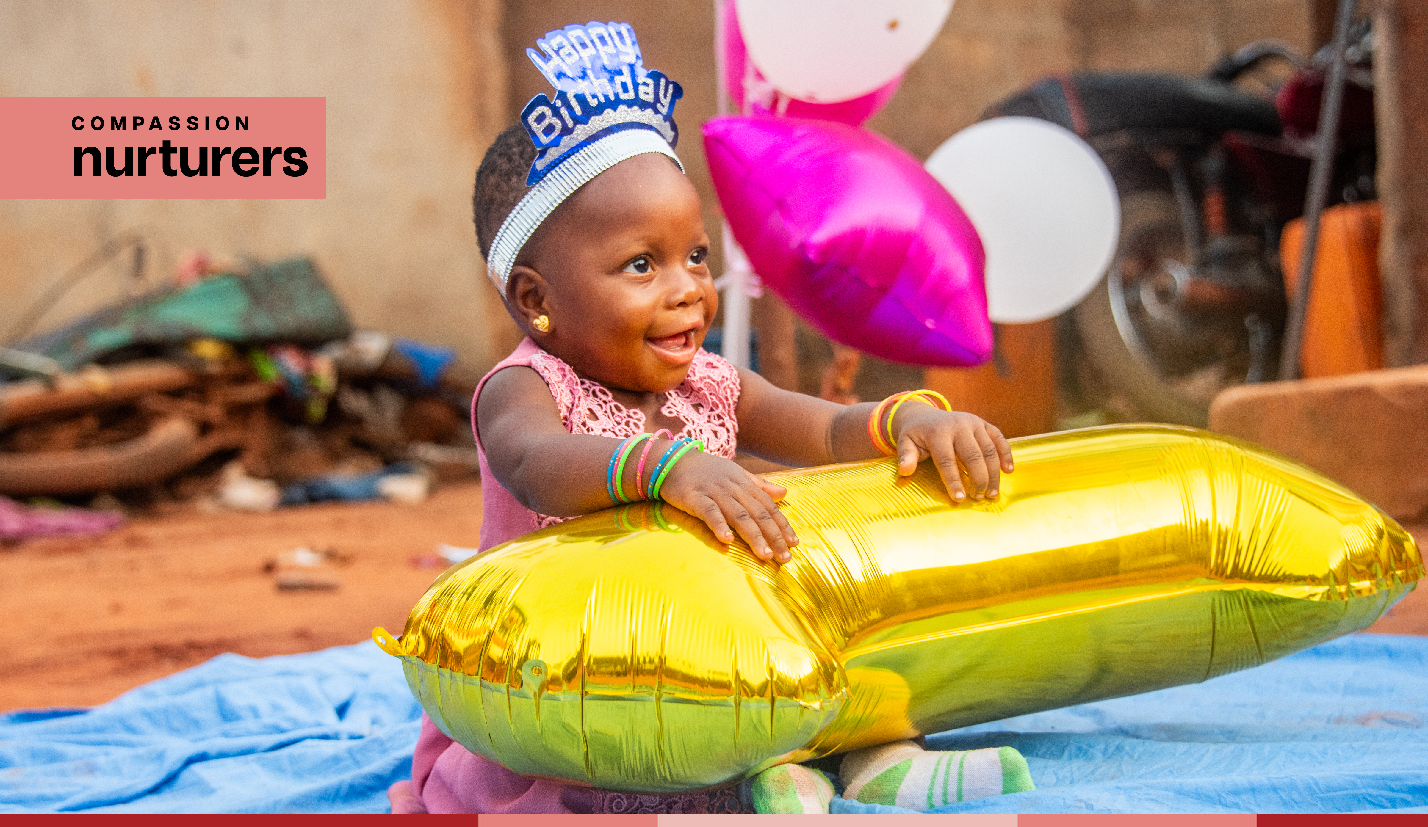 One year old Yawa smiles at her birthday party while holding a number-shaped balloon