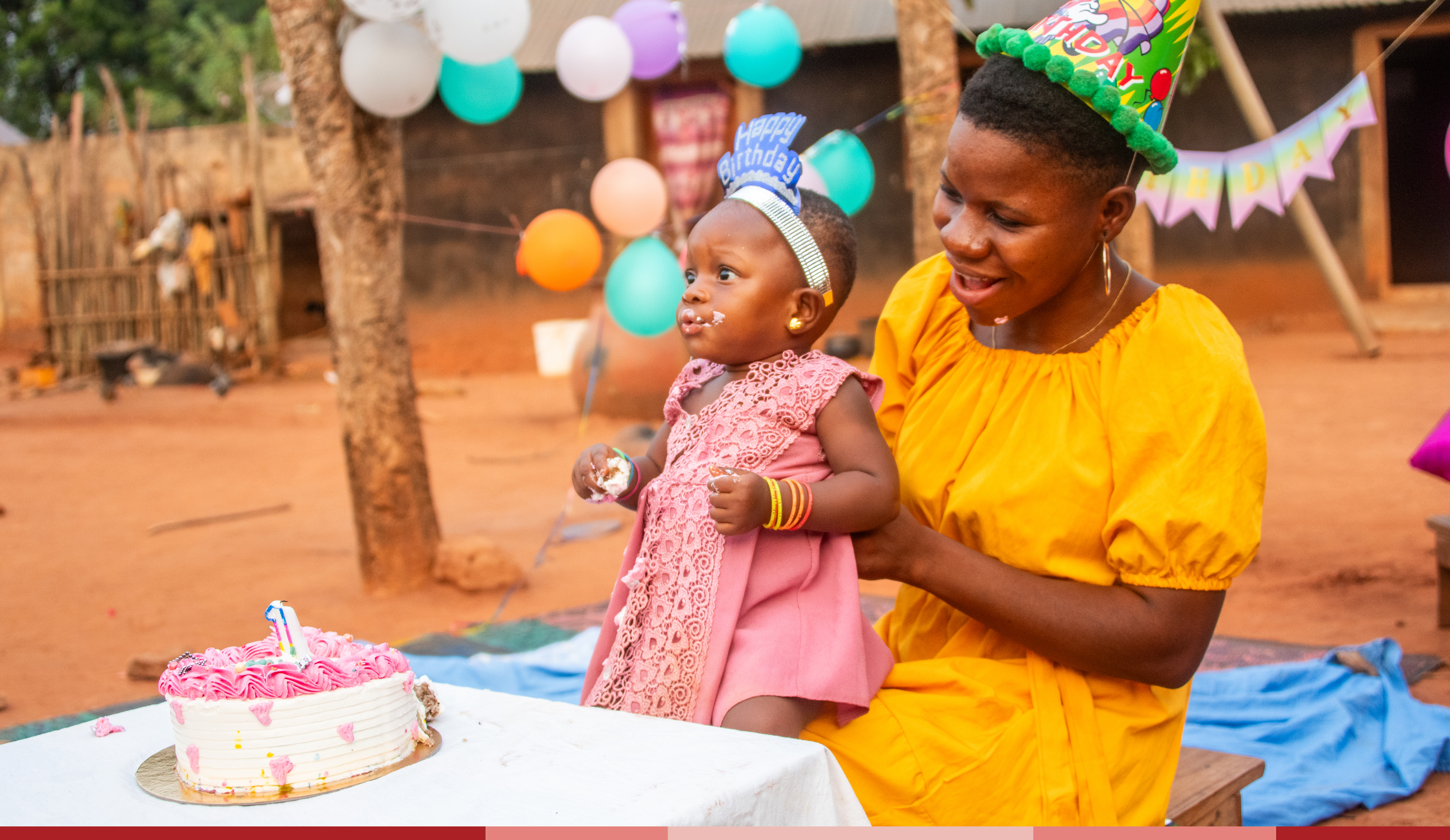 Davi is wearing a yellow dress and holds Yawa who is eating birthday cake