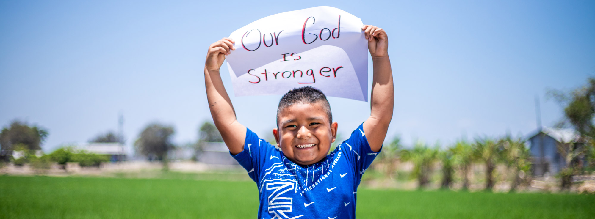 Little boy holding up "our God is stronger" sign