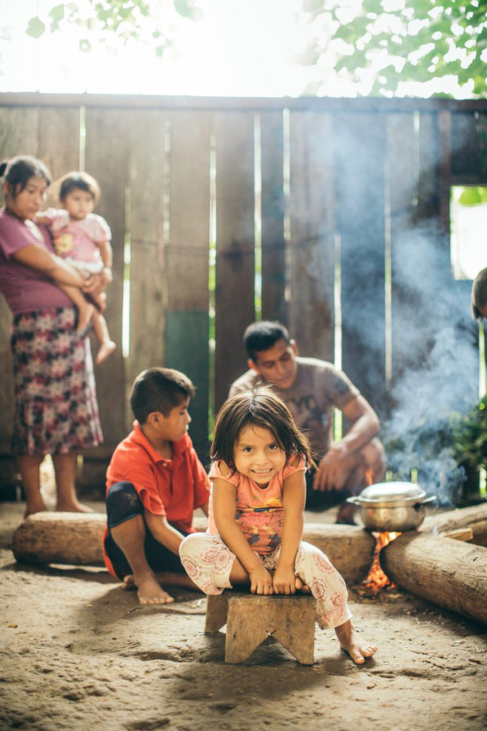A girl smiles with her family in the background near a small fire