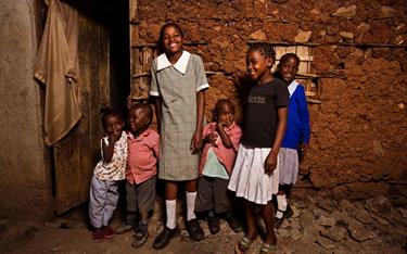 A teenage Kenyan girl and her siblings stand outside their home