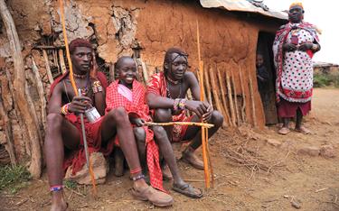 A Kenyan boy sits with two warriors from his village