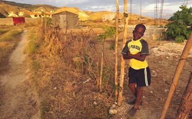 A boy stands in front of his family’s temporary shelter