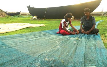 A girl helps her father mend a fishing net in eastern India