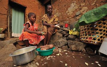 A girl and her mother peeling potatoes outside their home