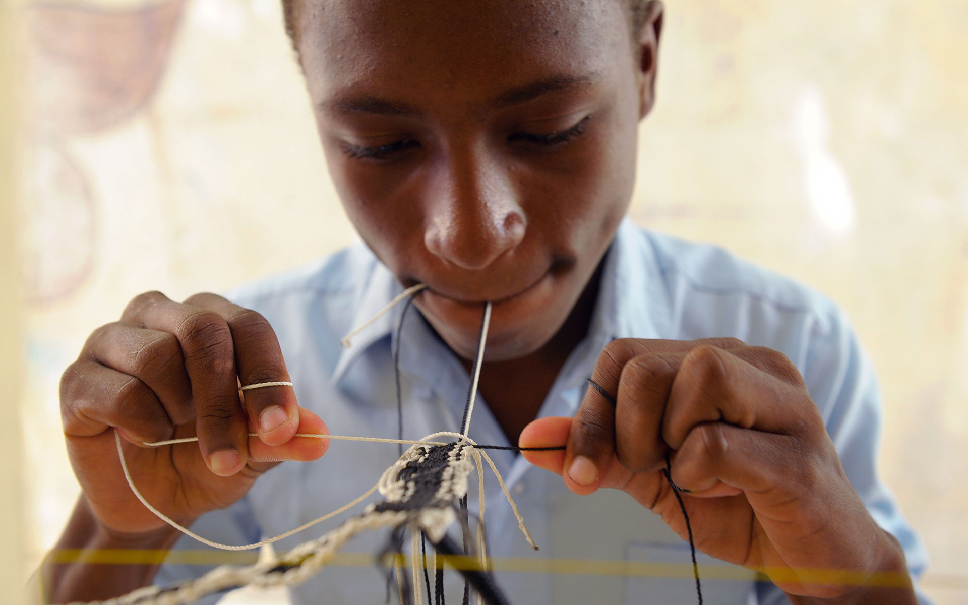 A boy from Haiti learns to tie macrame knots at his Compassion center