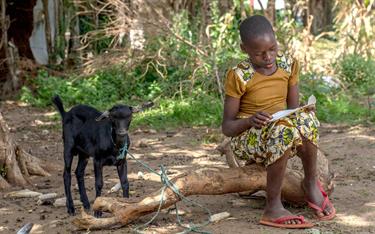 Salama reading sponsor letters while sitting next to a goat