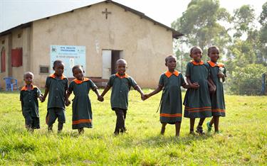 A group of children walks in the grass beside a Compassion center