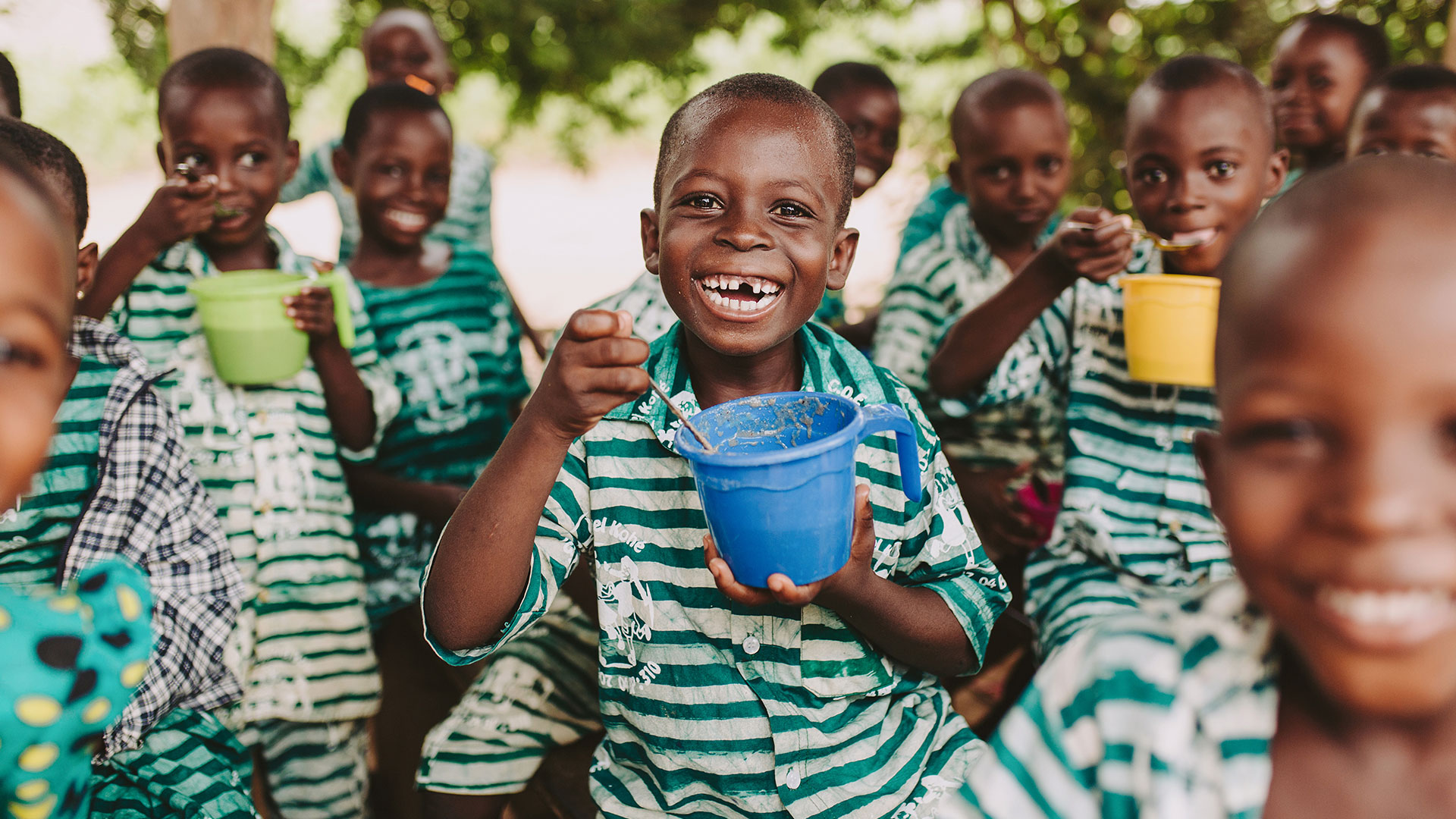 A group of children eat out of bowls and smile