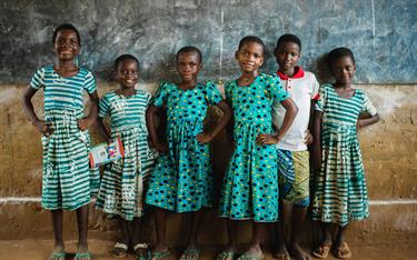 Sponsored children in Togo stand in front of the chalk board in their classroom
