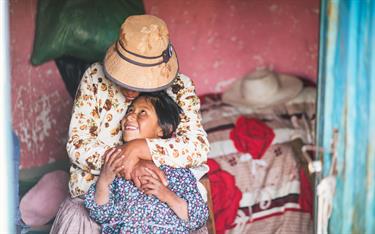 A girl in Compassion’s program snuggles up to her mom in their Bolivian home.