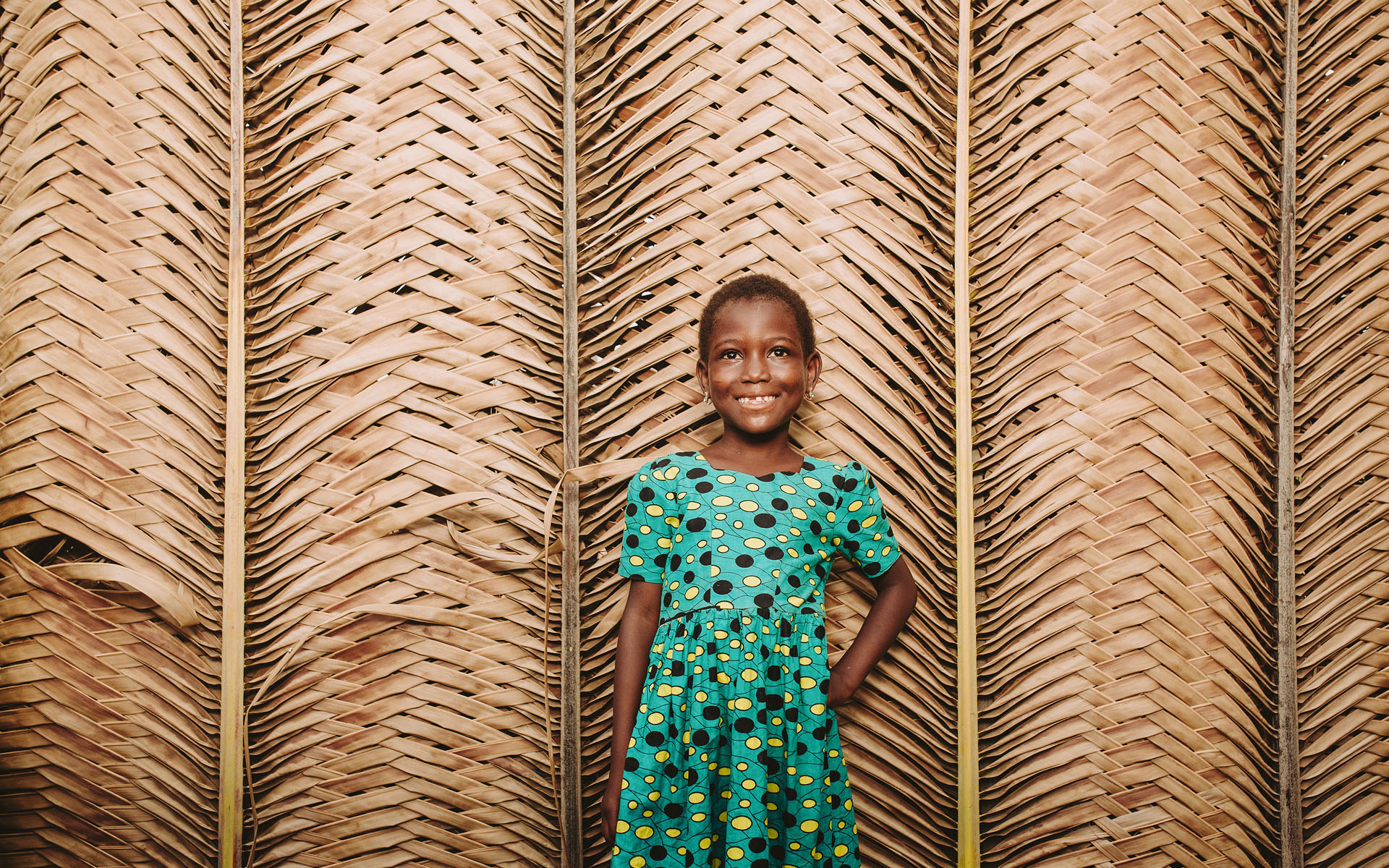 A girl in Togo wearing a green dress stands in front of a wall.