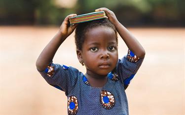 A toddler in Togo holding a book on his head