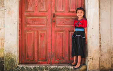 A young girl standing in front of a red door in Guatemala