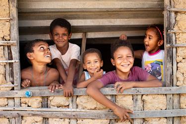 Children in Brazil look out a window in their house
