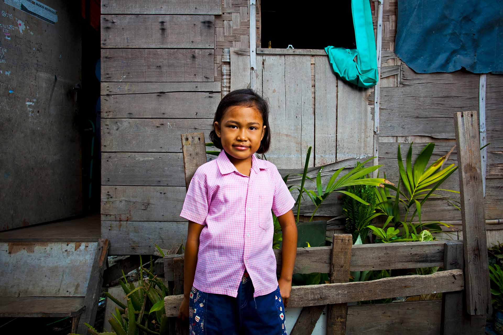 a girl stands outside of her home in Indonesia
